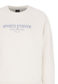Felpa beige chiaro con colletto a girocollo e maniche raglan. Presenta testo stampato blu: "SPORTS D'HIVER PISTE CHIC Protest." Texture liscia.