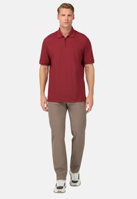 Czerwona koszulka polo z pół-zapięciem, krótkimi rękawami i kieszenią z przodu. Połączona z jasnobrązowymi spodniami i białymi trampkami.