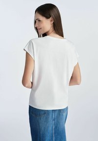 Biały krótki rękaw top z okrągłym dekoltem, wykonany z miękkiego materiału, w połączeniu z niebieską dżinsową spódnicą, prezentującą luźny krój i gładką fakturę.