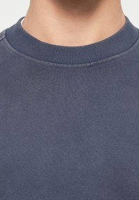 Σκούρο μπλε φούτερ με λαιμόκοψη, φτιαγμένο από μαλακή μίξη βαμβακιού, με ραμμένο κολλάρο και καθαρή ραφή στα μανίκια και στο στρίφωμα.