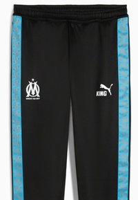 Czarne spodnie sportowe z elastycznym pasem. Niebieskie wzorzyste paski po bokach. Zawierają białe logo: Marseille i Puma.