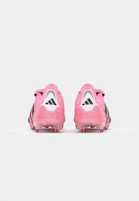 Roze sportieve voetbalschoenen met zwarte accenten, afgerond ontwerp, gestructureerd materiaal en doorzichtige zool met zichtbare noppen aan de onderkant.