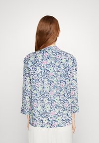 Hemd mit Knopfverschluss und langen Ärmeln, ausgestattet mit einem mehrfarbigen Blumenmuster auf hellem Hintergrund und einem dunkelblauen Rand. Glattes Material, lockere Passform.