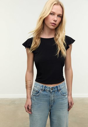 Schwarzes Kurzarmoberteil mit Rüschendetails, kombiniert mit hochgeschnittenen hellblauen Jeans. Verfügt über einen taillierten Schnitt und sichtbare Nähte.