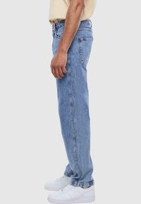Light blue denim jeans with a relaxed fit, straight leg design, five-pocket style, and a classic waistband, paired with white sneakers.