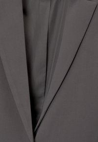 Gros plan sur le revers d'une veste de costume gris foncé montrant la texture du tissu et le détail de la doublure intérieure.