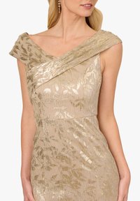 Beiges Kleid mit goldenen, schimmernden Blumenmustern, das über einen überkreuzten Oberteil und gerüschte Träger verfügt. Die glatte Textur verstärkt das Design.