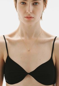 Bralette negro con un detalle frontal torcido, tirantes finos y una textura suave. Un delicado collar de oro presenta un pequeño colgante circular.