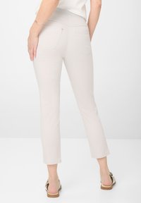 Pantalons ajustés beige clair avec une texture lisse, taille mi-haute et poches arrière. Ourlet court s'étend juste au-dessus de la cheville.