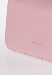 Portafoglio in pelle rosa con una texture liscia, angoli arrotondati e cuciture bianche. Presenta il logo del marchio debossato "aunts&uncles."