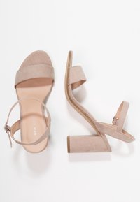 Beżowe zamszowe sandały na słupku z szerokimi paskami i klamrą na kostce. Gładka tekstura, odkryty palec, wysokość obcasa 4 cm, minimalistyczna estetyka.