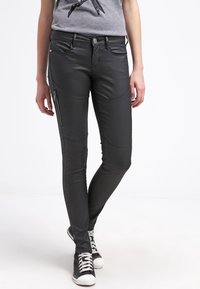 Černé kalhoty z umělé kůže se zipovými kapsami, slim fit a švy na nohavicích, spárované s šedým tričkem a černými teniskami.