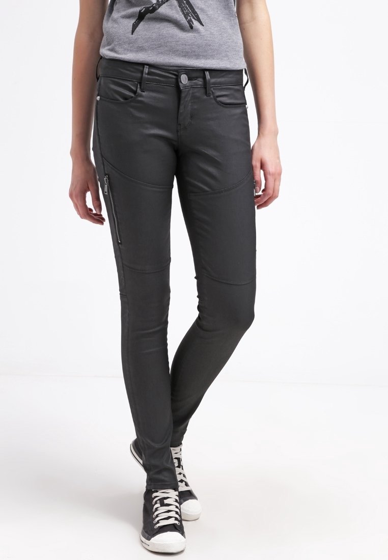 Černé kalhoty z umělé kůže se zipovými kapsami, slim fit a švy na nohavicích, spárované s šedým tričkem a černými teniskami.