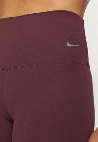 Bordo tajice visoka struka s glatkom teksturom. Imaju sivi Nike logo na pojasu i precizan, uskim krojem.