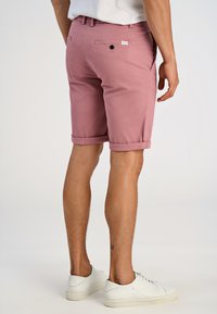 Pantaloni corti in cotone rosa chiaro con orli arrotolati, tasche posteriori e chiusura a bottone, abbinati a sneaker bianche in pelle. Design semplice e sartoriale.