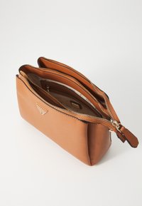 Poche en synthétique marron avec fermeture éclair, dotée de deux compartiments, avec une surface texturée et une quincaillerie dorée. L'intérieur comprend un logo.