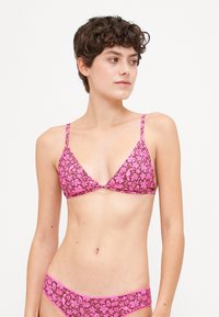 Biquíni triangular com padrão floral rosa sobre fundo castanho escuro. Tiras finas, parte de baixo de cintura baixa combinando, textura suave. Sem metal visível.