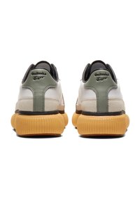 Tenisky Onitsuka Tiger s bílým koženým svrškem, zelenými akcenty, černým podpatek a silnou, strukturovanou gumovou podrážkou.