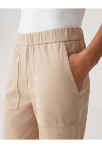 Pantalons beige à taille élastique avec poches latérales, texture lisse et détails de couture subtils. Gros plan montrant la taille et la zone des poches.