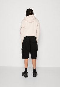 Jasno beżowy hoodie z kapturem i różowymi akcentami, zestawiony z czarnymi szortami cargo z bocznymi kieszeniami, noszonymi z czarnymi skarpetami i butami.