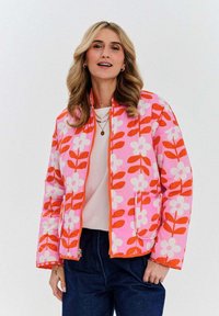 Ružová prešívaná bunda s kvetinovým vzorom v bielej a oranžovej farbe. Uzatváranie na zips a bočné vrecká. Kombinovaná s ľahkým topom a tmavými džínami.