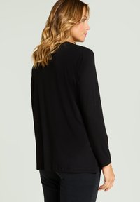 Schwarzes Langarmoberteil aus einem glatten, leichten Stoff mit lockerer Passform und abgerundetem Saum. Einfaches Design ohne Muster oder Verzierung.