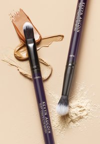 Kevyn Aucoin Duet Concealer Brush mit beidseitigem Design; eine Seite hat spitze schwarze Borsten, die andere dichtes weißes Borsten. Zwei Foundation-Swatches.