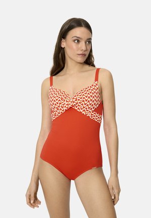 Mujer con un traje de baño de una pieza rojo, con un patrón de zigzag en rojo, blanco y amarillo en el busto, posando frente a un fondo liso.