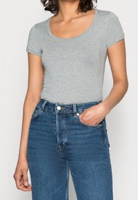 Šedé krátké tričko s krátkým rukávem a kulatým výstřihem, kombinované s modrými džínami s vysokým pasem a klasickým designem s pěti kapsami.