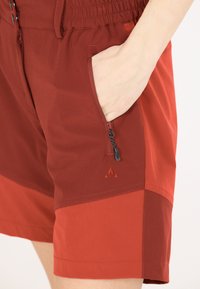Punaiset shortsit, joissa on joustava vyötärö, sivutasku vetoketjulla ja pieni logo. Valmistettu kevyestä kankaasta, jossa on kontrastisia tekstuureja.