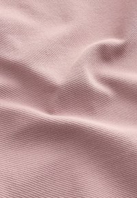 Lys pink tekstureret stof med et ribbet mønster, der viser blide folder og kurver, som antyder blødhed og fleksibilitet.