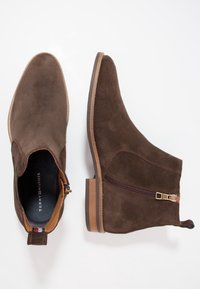 Stivaletti in suede marrone con punta smussata e liscia, zip laterale e accenti in tonalità tan. Presentano un tacco basso impilato e una parte superiore testurizzata.