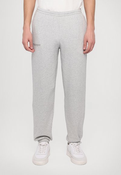 Grå sweatpants med elastisk talje, taperede manchetter og en diskret tekstdetalje på venstre lår. Sammen med hvide sneakers.