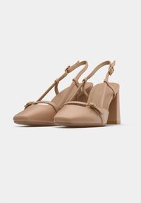 Escarpins slingback nude à bout pointu, avec bride ornée et accents en métal doré. Ils présentent un talon carré et une texture lisse.