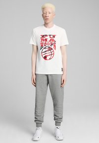 Hvid bomulds T-shirt med rød grafisk tryk, der indeholder tekst og et basketballmotiv, parret med grå sweatpants og hvide sportsko.