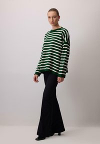 Green and white striped knit sweater with a loose fit and long sleeves, paired with black flared pants and pointed shoes.