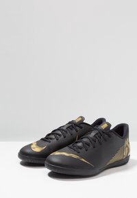 Schwarze Sportschuhe mit einer strukturierten Oberseite, ausgestattet mit einem goldenen Nike-Swoosh und Akzentlinien; Schnürdesign; niedriges Profil.