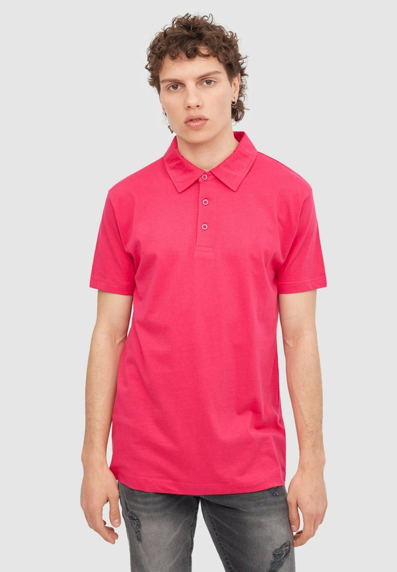 Camisa polo rosa de mezcla de algodón que presenta un cuello clásico, tapeta de tres botones y mangas cortas, combinada con jeans de mezclilla de lavado piedra.