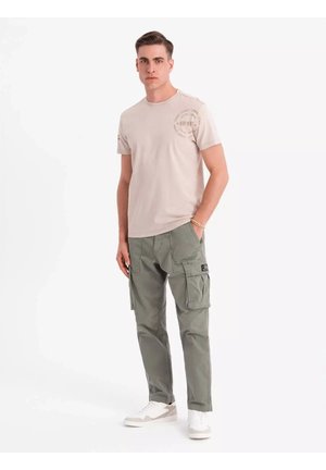 Lys beige t-shirt med rund hals og trykt design. Olivenfarvede cargo bukser med flere lommer, båret med hvide sneakers.