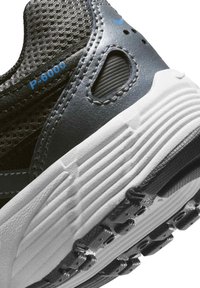 Κοντινή λήψη στη φτέρνα ενός αθλητικού παπουτσιού σε μαύρο και γκρι χρώμα με λευκή υφή στη σόλα και μπλε κείμενο "P-6000" σε πλέγμα ύφασμα.