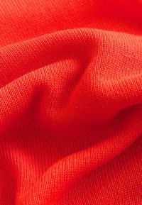 Gestrickter Stoff in lebendigem Rot, mit weicher Textur und feinen Rippungen. Das Material zeigt einen leichten Glanz und fällt fließend.