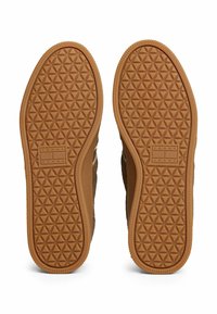 Suola di scarpa in gomma con un motivo testurizzato a triangoli, di colore marrone chiaro, e un'area di marca contrassegnata con "TOMMY JEANS."