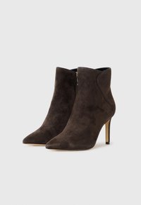 Botas de ante marrón hasta el tobillo con puntera afilada y tacón stiletto alto. Detalle de cremallera en el lateral con una textura suave y una silueta elegante.