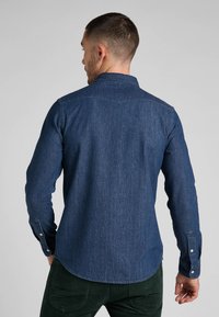 Sötétkék farmering, klasszikus gallérral, gombos mandzsettával és ívelt paszománnyal. Puha textúra sima felülettel.