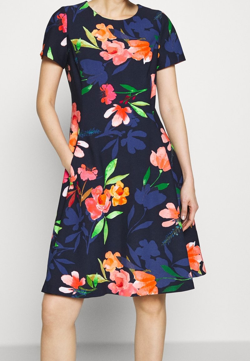 Robe à motifs floraux avec des manches courtes, fond marine, fleurs roses vives, orange et vert, longueur genoux, avec poches latérales.