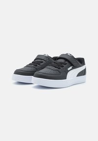 Baskets synthétiques noires avec semelle blanche, présentant un système de fermeture à lacets et sangle, des détails perforés et un accent logo sur le côté.