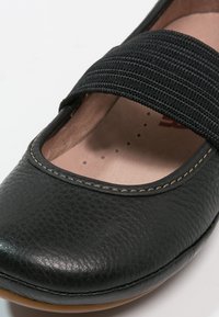 Schwarzer Leder-Mary-Jane-Schuh mit elastischem Riemen und sichtbaren Nähten entlang der Zehen und Seiten.