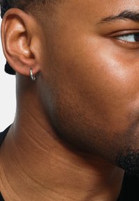 Boucle d'oreille en argent sur une oreille rasée de près. Peau lisse avec une texture subtile, mettant en valeur le design circulaire de la boucle contre un fond sombre.
