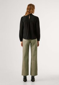 Zwarte blouse met lange mouwen en een keyhole detail aan de achterkant, gecombineerd met lichtgroene wijde pantalon en zwarte heeled boots.