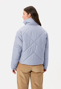 Giacca a vento azzurro chiaro con collo alto, design trapuntato e polsini elastici. Indossata sopra pantaloni di velluto a coste color beige, con una vestibilità comoda.